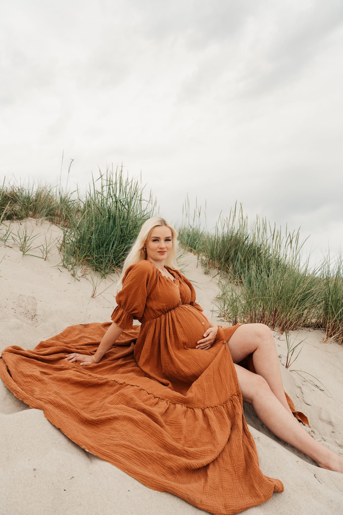 Schwangere im rostfarbenen Kleid in den Dünen am Meer
