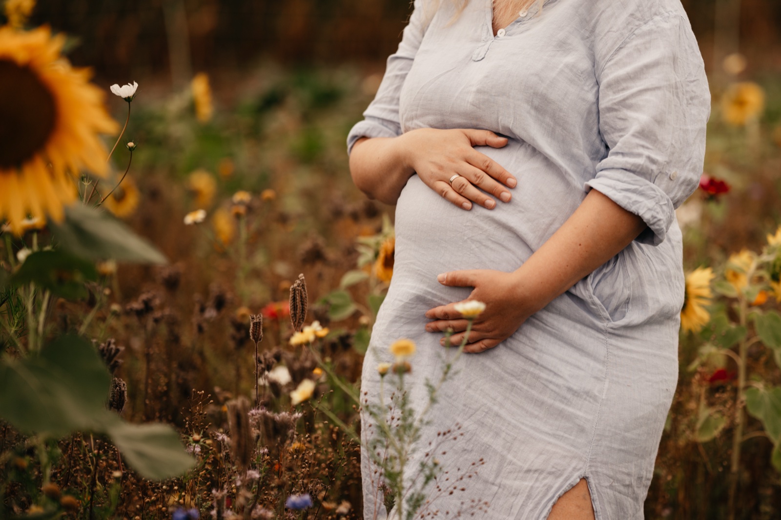 Schwangere hält ihren Bauch, im Vordergrund blühende Sonnenblumen