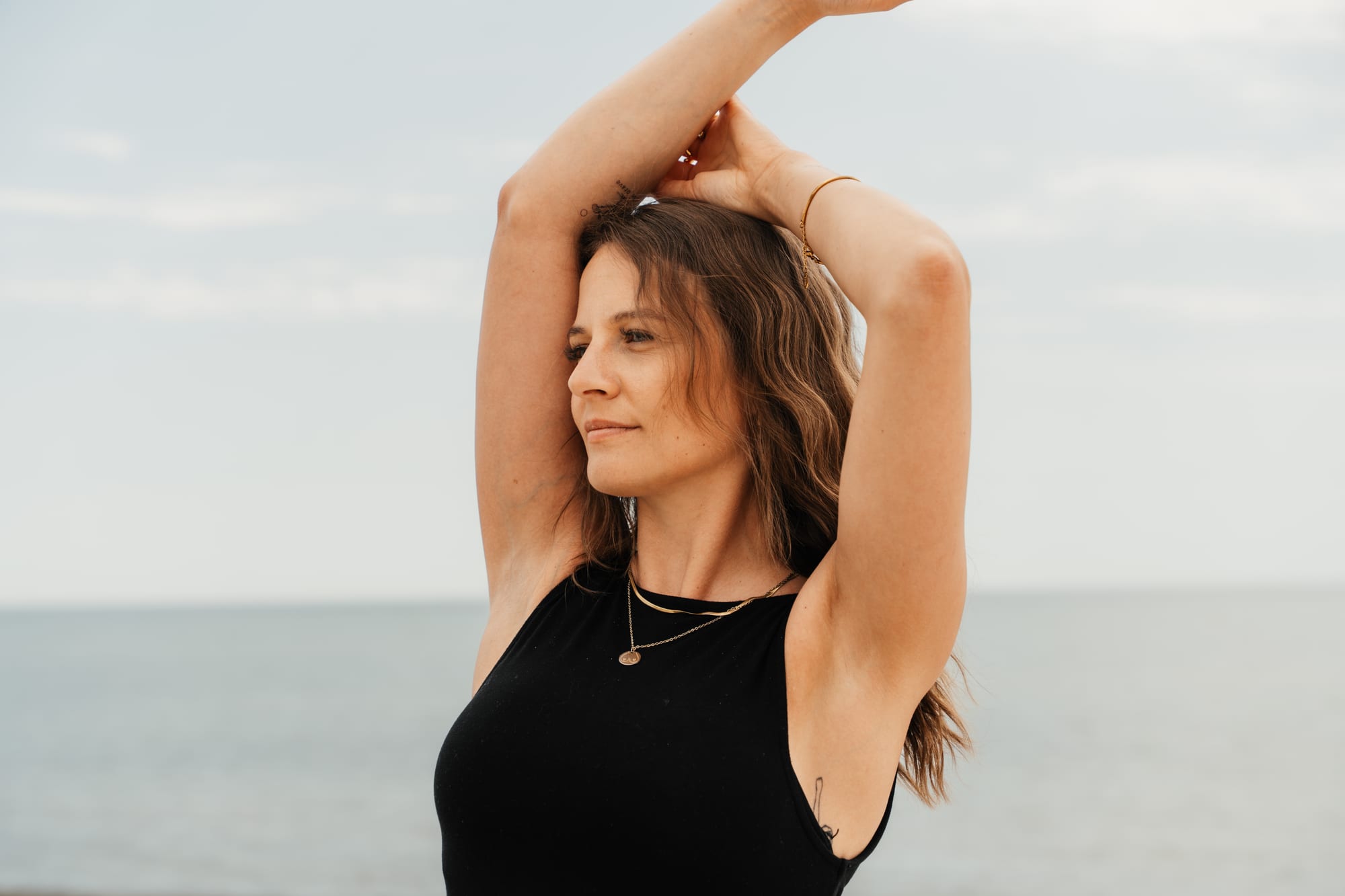 Lena rahmt ihr Gesicht mit den Armen, das Meer im Hintergrund